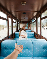 A woman poses smiling in a vintage train car while shaking hands with the photographer on the end...