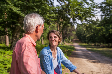 Happy caucasian woman looking at her mature father with love while riding bicycles