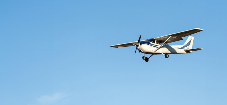 Small white plane with blue stripes of a cessna propeller flying in the evening light in a clear blue sky before landing at Sabadell airport. - Powered by Adobe