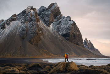 A tourist couple stands on the beach, admiring the majestic reflection of the Vestrahorn mountain...