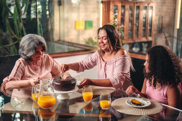 Mulher Brasileira servindo bolo para sua mãe e sua filha na mesa de durante almoço de dia das...