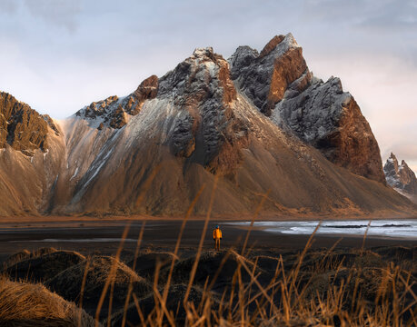 A tourist  stands on the beach, admiring the majestic reflection of the Vestrahorn mountain at Cape Stokksnes, Iceland, as the sun rises on the horizon. The beautiful snow-capped mountains.