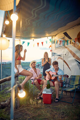 Friends in front of camper rv. Man playing guitar. Summertime fun and togetherness. Travel, holiday, weekend, lifestyle concept. - 611292241