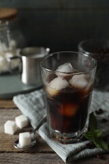Glass of delicious iced coffee, mint and sugar cubes on wooden table