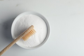 Bamboo toothbrush and bowl of baking soda on white marble table, top view. Space for text