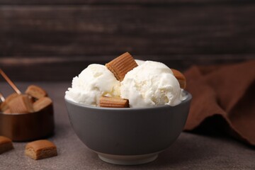 Scoops of ice cream with caramel candies in bowl on textured table, closeup