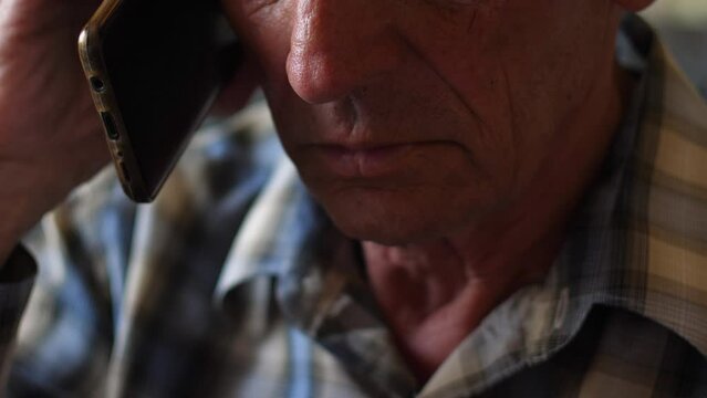 The Face Of A Sad Pensioner Listening To The Speech Of The Interlocutor On The Phone. A Real Pensioner Communicates On The Phone. An Elderly Father With A Telephone