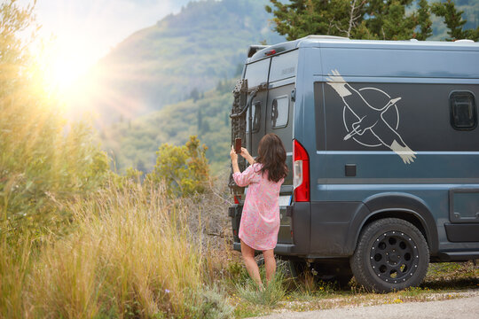 Work and Travel concept, outdoor leisure activity and wanderlust lifestyle - woman next to off road camper van taking pictures by mobil phone of sunset. Spring time, Greece, Lefkada Island.
