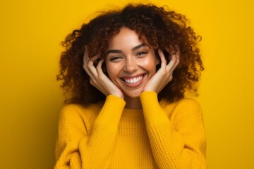 Headshot portrait photography of a grinning girl in her 20s making a heart with the hands against a bright yellow background. With generative AI technology