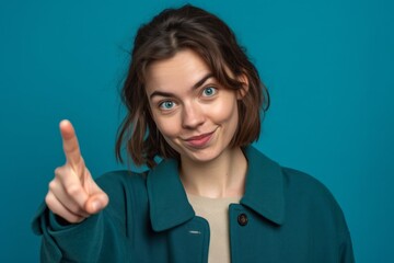 Close-up portrait photography of a satisfied girl in her 20s making a i see you gesture pointing at one's eyes against a teal blue background. With generative AI technology