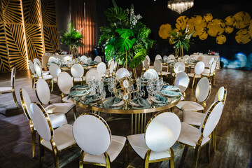 Round served banquet tables ready for guests, decorated table with plate, glasses, forks, emerald...
