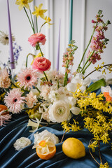 Summer composition of garden flowers. Festive decorated with flowers, fruits, greenery, candles. Bouquet in vase, and orange, lemon on table. Home interior with decor spring elements. Details closeup
