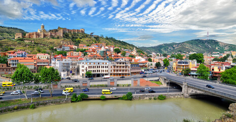 Picturesque Panorama of the old town of the capital of Georgia, the city of Tbilisi in summer sunny day. Kura river, Metekhi bridge, ancient Narikala fortress and colorful old buildings in Tbilisi - obrazy, fototapety, plakaty
