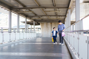 Happy cheerful Asian little boy and his father walking in the city with carrying a colorful paper shopping bag, father and son walking together in the city or downtown.