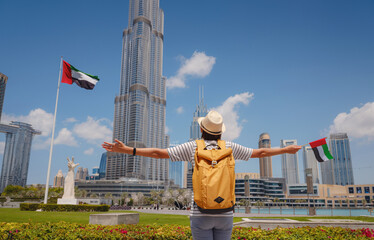 Enjoying travel in United Arabian Emirates. Young woman with yellow backpack with the flag of the...