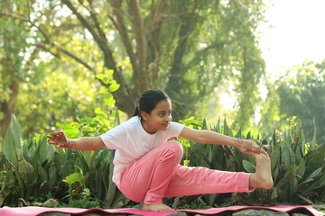 Young Indian female child practicing  yoga in the park in day time. Girl is doing yoga in clean and green environment and fresh air.