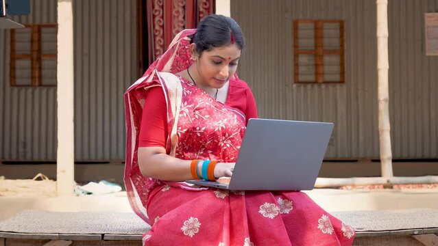 Indian rural woman uses technology, sitting outside her modest home, connecting to the online world for work. Women empowerment with technology. Online banking and payments.
