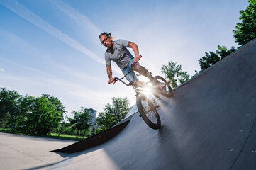 Low angle view of a mature tattooed man riding a bmx bike on a ramp in a skate park.