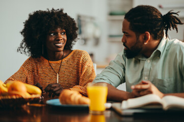 An african american man is sitting with his wife at the breakfast table at home and talking to her.