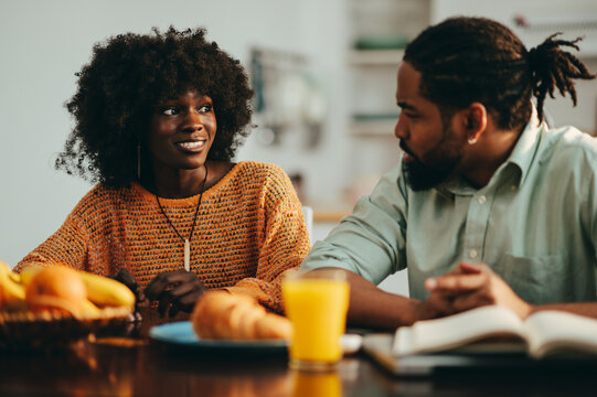 An african american man is sitting with his wife at the breakfast table at home and talking to her.