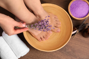 Woman holding lavender flowers and soaking her foot in bowl with water, top view. Pedicure procedure