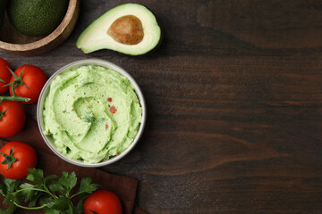 Bowl of delicious guacamole and ingredients on wooden table, flat lay. Space for text