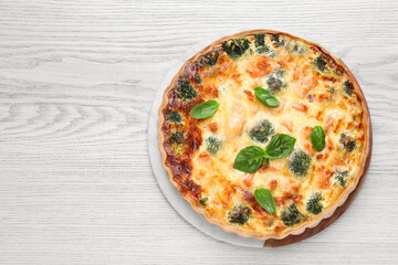 Delicious homemade quiche with salmon, broccoli and basil leaves on wooden table, top view. Space for text