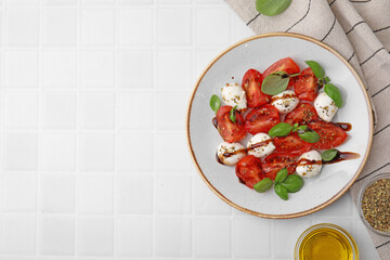 Tasty salad Caprese with mozarella balls, tomatoes, basil and other ingredients on white tiled table, flat lay. Space for text