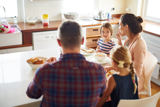Happy family, morning and eating breakfast on kitchen for meal or bonding time together at home. Mother, father and children with healthy food to start the day for nutrition or cereal in the house
