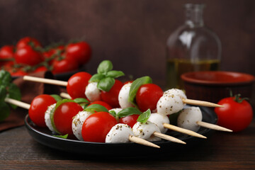 Delicious Caprese skewers with tomatoes, mozzarella balls, basil and spices on wooden table, closeup