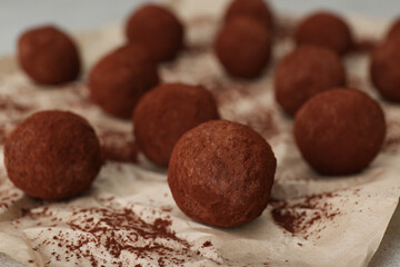 Delicious chocolate candies powdered with cocoa on parchment paper, closeup