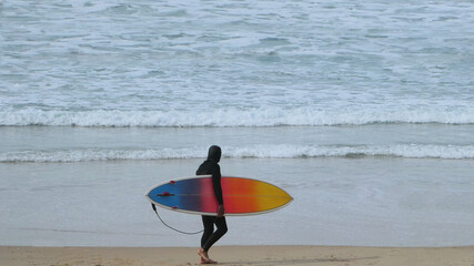 man carrying rainbow colored surfboard walking on sand at the beach