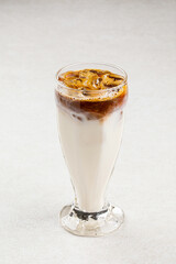 Glass of cold coffee with ice and milk on light background
