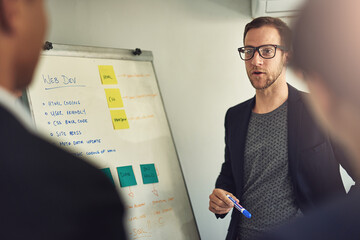 Web design, manager with team, man and a whiteboard planning in a business meeting in modern office or startup together. Teamwork or collaboration, developer group or ideas and colleagues in workshop