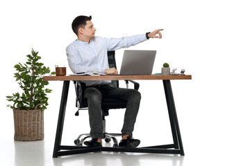 young man using laptop at table and pointing at copy space