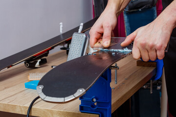 Hands scrape wax off ski with scraper in workshop