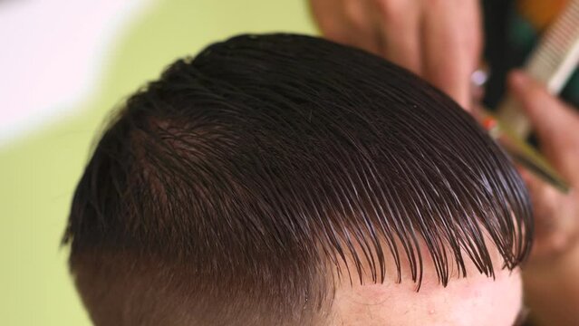 hairstylist with scissors and a comb create a straight fringe for a young man