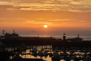 Fototapeta na wymiar The sun rises in an orange sky over the silhouette Ramsgate harbour