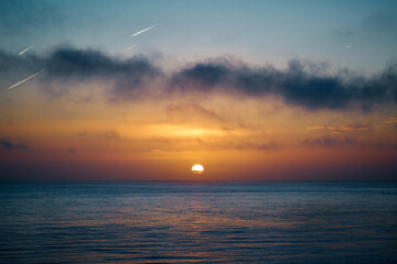 The sun rises over the a calm sea with dark clouds in the foreground