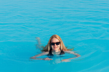 An attractive woman swims in an outdoor pool in the morning in the sun. The concept of an expensive holiday