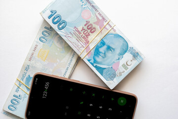 A pack of 100 Turkish lira banknotes and a calculator on a smartphone. A stack of 100 Turkish lira banknotes and a smartphone on a light background.