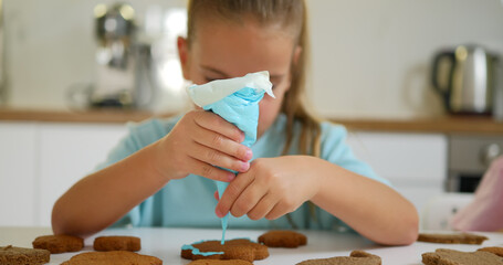 Little girl decorate ginger cookies for the holiday at home.