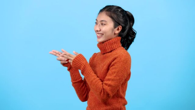 Portrait cute Asia girl looking camera pointing or presenting on blue background, smiling woman in colorful warm sweater show gun fingers 2 hands with happy for shopping advertisement concept