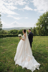 Portrait of the bride and groom in nature. A stylish bride and groom in a long lace dress are walking in the garden holding hands. Couple in love