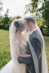 A curly-haired brunette bride in a white dress and a veiled groom embrace and kiss. Portrait of the...
