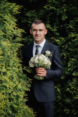 A man in a black suit poses in nature with a bouquet. A stylish watch. Men's style. Fashion....