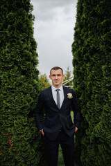 A man in a black suit poses in nature, near conifers. A stylish watch. Men's style. Fashion....