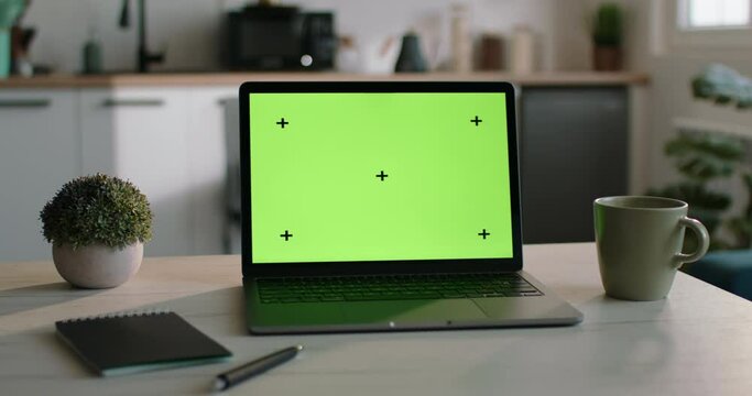 A cinematic frame with a laptop mockup on the kitchen table. A laptop mockup with a green display, a template for inserting any of your material into the green laptop screen on the kitchen table.