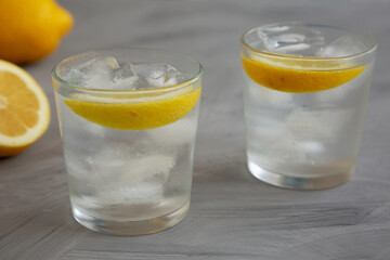 Refreshing Cold Water with Lemon in Glasses on gray background, side view. Close-up.