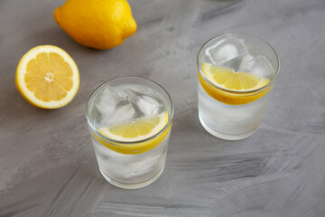 Refreshing Cold Water with Lemon in Glasses on gray background, side view.
